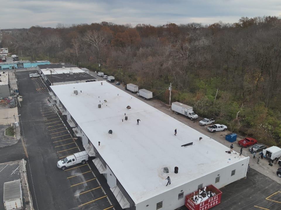Aerial view of a freshly installed white TPO roof on a long commercial building in the St. Louis metro, with the Amigo crew on the roof and trucks parked below